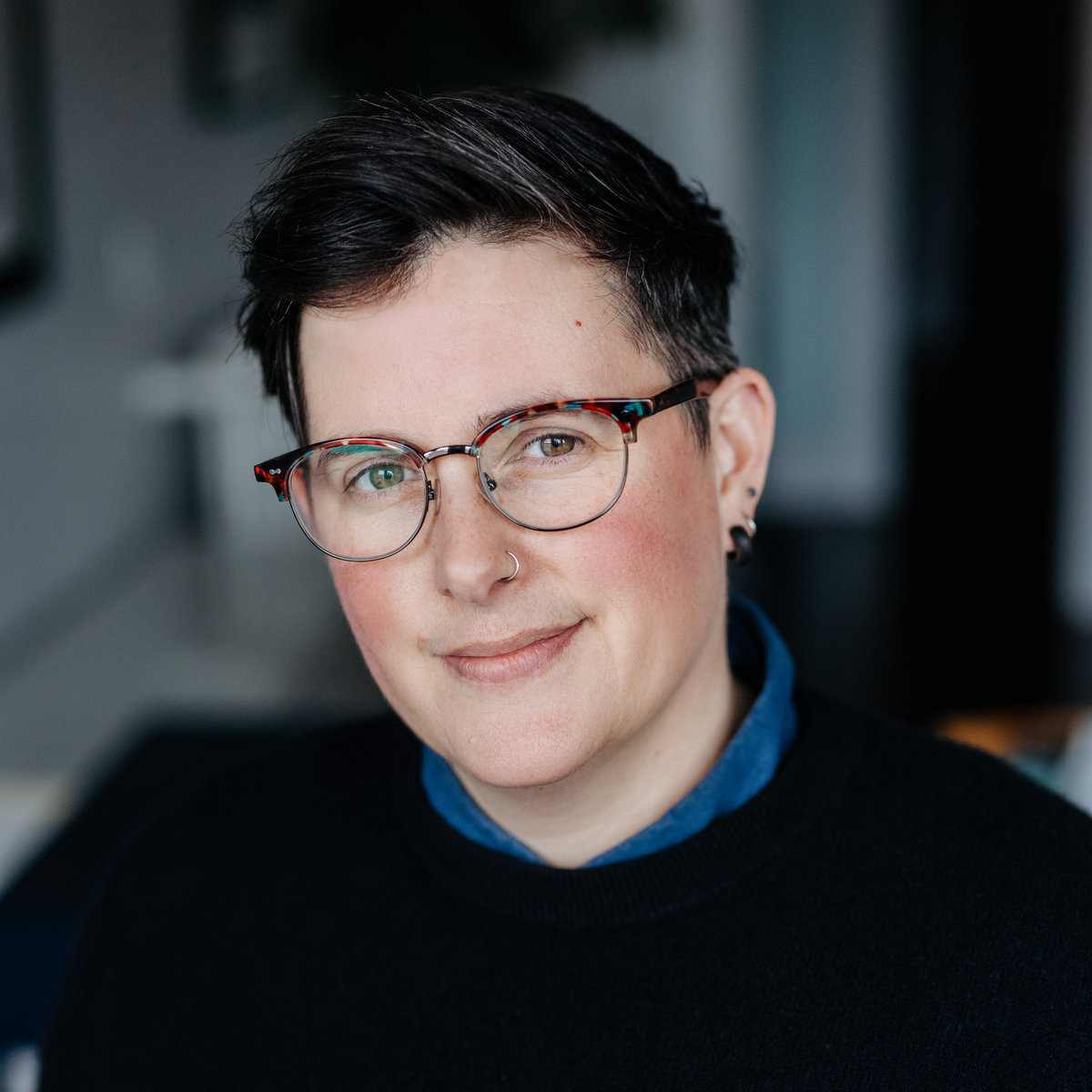 Morgan Brooks from the shoulders up, smiling at the camera, wearing glasses and a black sweater